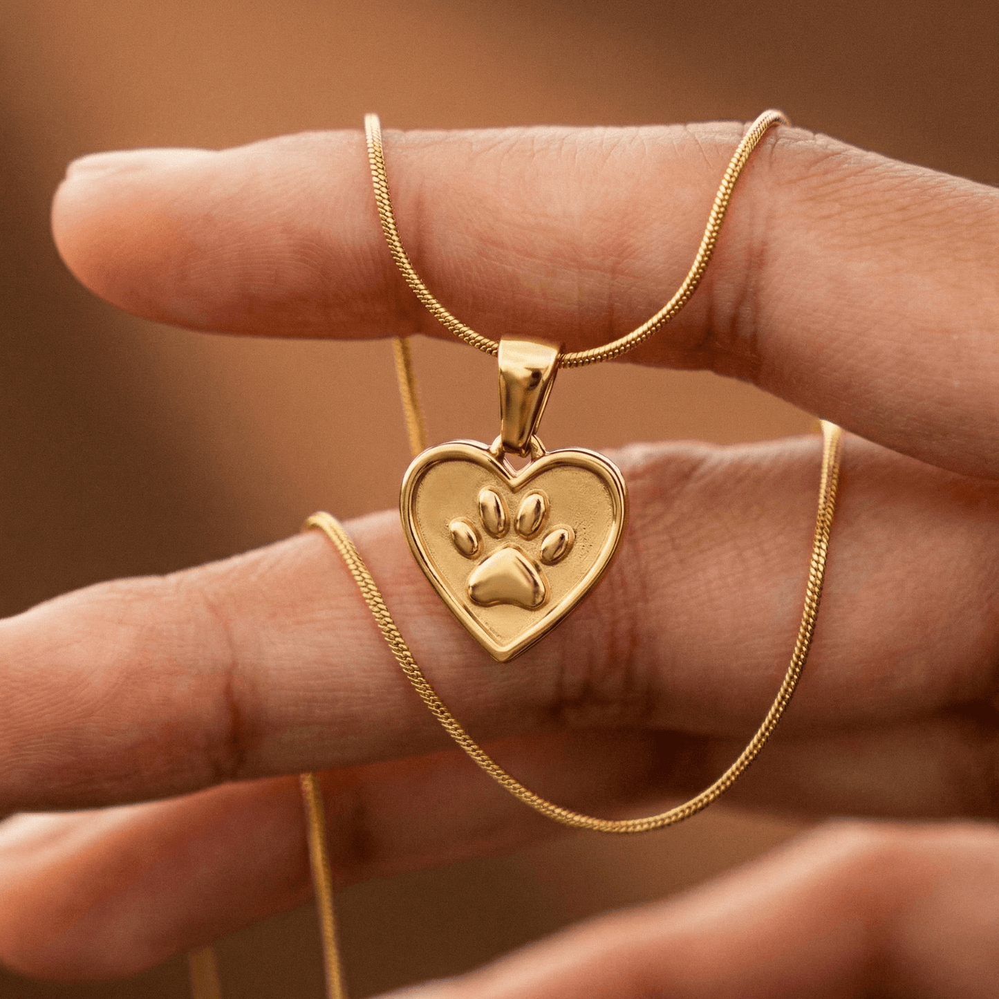 Gold paw and heart pendant dog charity necklace held in hand, helps fund 30 shelter dog meals